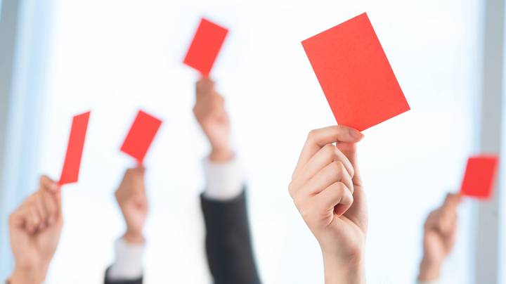 Abstimmungsverfahren in einer Vertreterversammlung: Fünf Hände halten eine rote Karte in die Luft