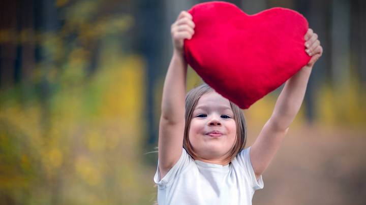 Ein kleines Mädchen hält ein rotes Herz aus Plüsch in die Höhe
