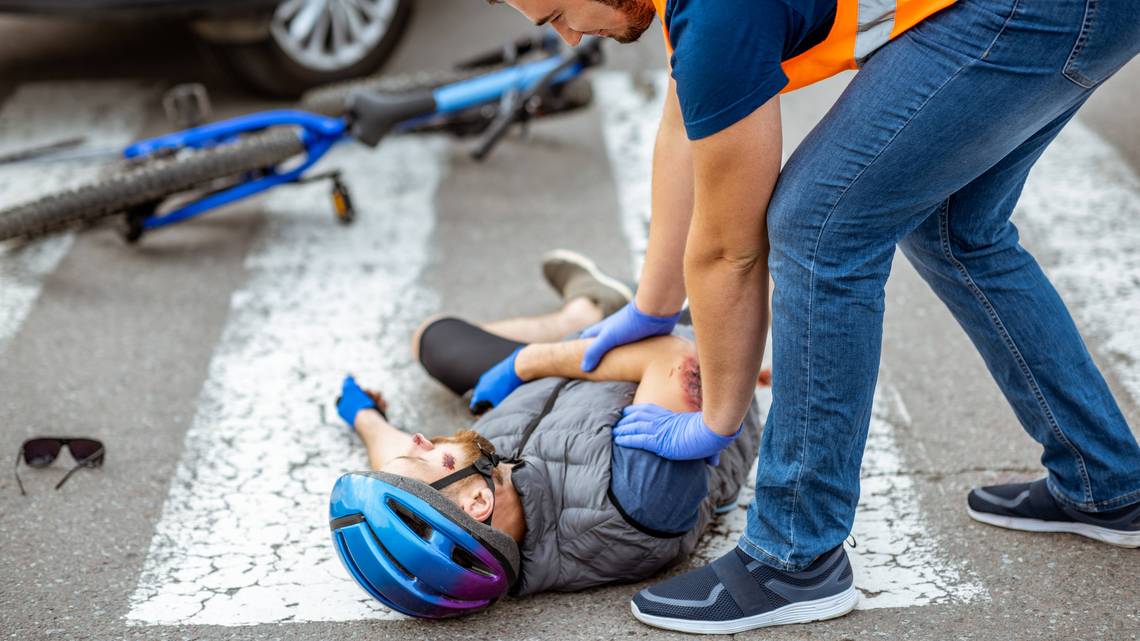 Ein Ersthelfender versorgt einen verletzten Radfahrer